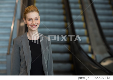 Businesswoman standing and smiling in lobby near escalators with metal handrails, copy space Businesswoman standing and smiling in lobby near escalators with metal handrails, copy space 135307218
