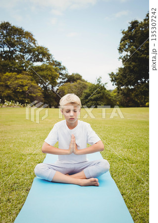 Boy meditating cross-legged on bright blue yoga mat in park pressing hands at chest 135307242