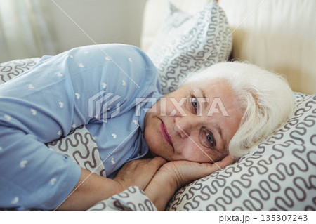 Senior woman wearing heart patterned pajamas lying in bed resting head on pillow Senior woman wearing heart patterned pajamas lying in bed resting head on pillow 135307243