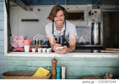 Man leaning forward at street-side food truck window while holding notepad and pen near red napkins Man leaning forward at street-side food truck window while holding notepad and pen near red napkins 135307244