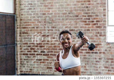 African American woman punching with dumbbell and pink wrist wrap in fitness studio African American woman punching with dumbbell and pink wrist wrap in fitness studio 135307255