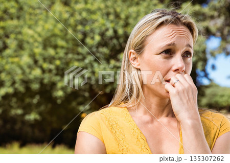 Middle-aged woman biting nails at park wearing yellow lace top with silver ring, copy space Middle-aged woman biting nails at park wearing yellow lace top with silver ring, copy space 135307262