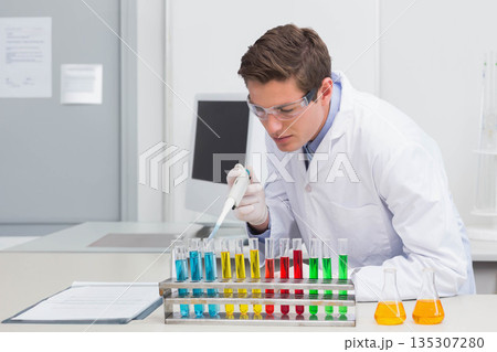 Adult male scientist using pipette depositing liquid into test tube rack on lab bench with flasks 135307280
