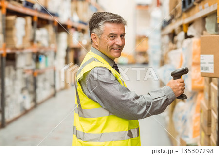 Male warehouse worker scanning boxes with handheld barcode scanner inside aisle wearing safety vest Male warehouse worker scanning boxes with handheld barcode scanner inside aisle wearing safety vest 135307298