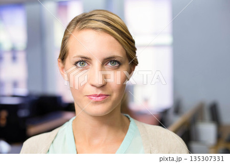 Professional woman standing in open office wearing cardigan over blouse with desks and windows 135307331