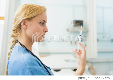 Female medical professional inspecting syringe in clinic with stethoscope near bed, copy space 135307369