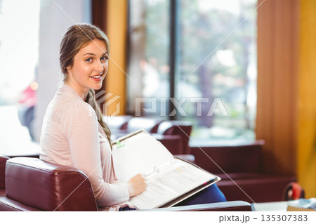 Woman reading open binder while sitting on leather lounge chair in study area, copy space 135307383