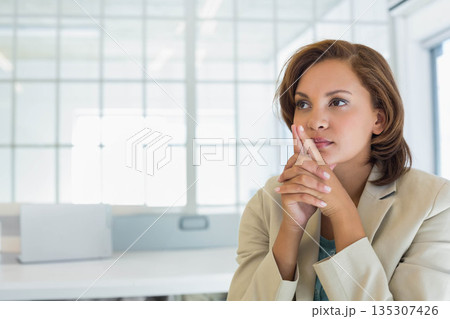 Hispanic woman in blazer sitting at office desk gazing left by grid windows, monitor, copy space Hispanic woman in blazer sitting at office desk gazing left by grid windows, monitor, copy space 135307426