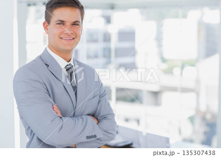 Businessman wearing grey suit and tie standing arms crossed in office by windows, copy space 135307438