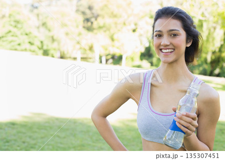 Asian woman holding clear water bottle standing on sunny park field in workout wear, copy space 135307451