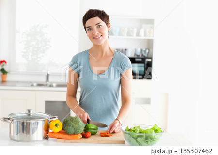 Mid adult woman slicing vegetables on cutting board near glass bowl, stainless pot in home kitchen 135307462