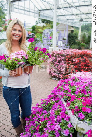 Woman holding two terra cotta pots with pink petunias, standing under greenhouse canopy, copy space 135307526
