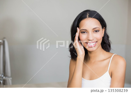 African American woman smiling and touching cheek at bathroom sink with chrome faucet, copy space African American woman smiling and touching cheek at bathroom sink with chrome faucet, copy space 135308239