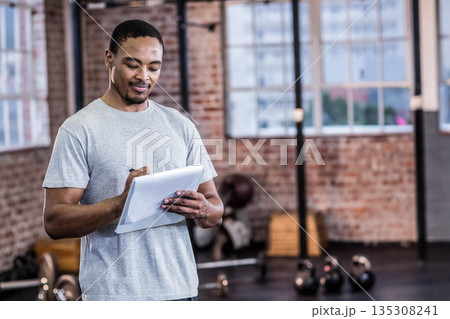 African American man holding tablet and stylus while tracking kettlebell workouts in brick gym African American man holding tablet and stylus while tracking kettlebell workouts in brick gym 135308241