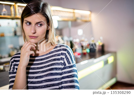 Woman leaning on counter resting chin on hand while gazing right at bar glassware bottles Woman leaning on counter resting chin on hand while gazing right at bar glassware bottles 135308290