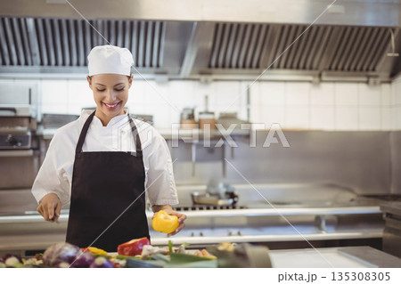 Native American woman chef slicing yellow pepper at counter in professional kitchen, copy space Native American woman chef slicing yellow pepper at counter in professional kitchen, copy space 135308305