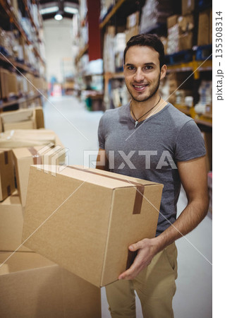 Man wearing grey shirt holding sealed cardboard box in warehouse aisle with shelving, copy space 135308314