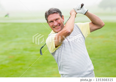 Senior African American man swinging golf club on fairway wearing striped polo shirt and glove 135308315