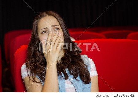 Woman in denim vest over striped tee covering mouth sitting in red theater chairs, copy space 135308342