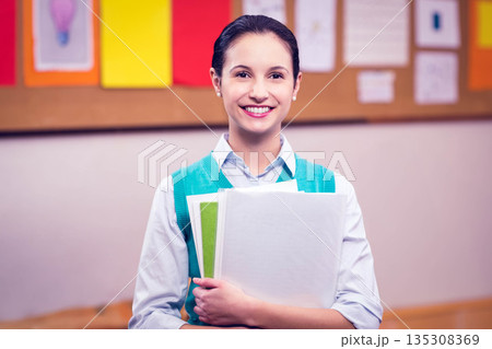 Female student in turquoise vest holding papers and notebooks before classroom bulletin board Female student in turquoise vest holding papers and notebooks before classroom bulletin board 135308369