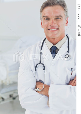 Diverse coworkers wearing lab coats standing in clinical room near hospital bed with stethoscope Diverse coworkers wearing lab coats standing in clinical room near hospital bed with stethoscope 135308451