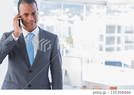 African American man holding smartphone to ear and making call in bright office space, copy space 135308460