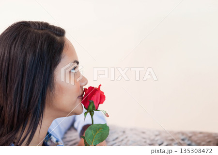 Woman smelling red rose while sitting on patterned sofa in living area, copy space Woman smelling red rose while sitting on patterned sofa in living area, copy space 135308472
