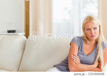 Woman sitting on fabric sofa in living room, crossing arms and gazing toward window, copy space Woman sitting on fabric sofa in living room, crossing arms and gazing toward window, copy space 135308489