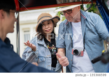Old white man thump up to driver aside wife after riding in tuk tuk three wheel taxi touring a city. Old white man thump up to driver aside wife after riding in tuk tuk three wheel taxi touring a city. 135308599