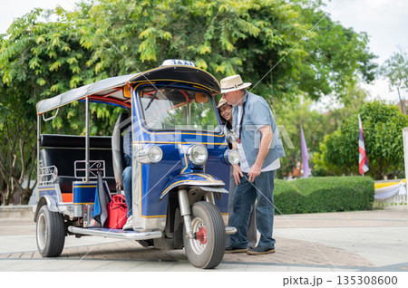 Old white man and wife talking to driver after riding in tuk tuk or three wheel taxi touring a city. Old white man and wife talking to driver after riding in tuk tuk or three wheel taxi touring a city. 135308600