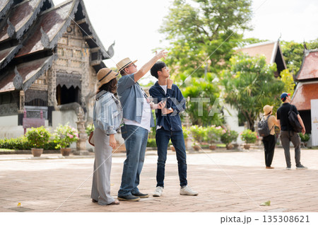 Old white man holding phone aside woman and guide standing and looking around buddhist temple ground Old white man holding phone aside woman and guide standing and looking around buddhist temple ground 135308621