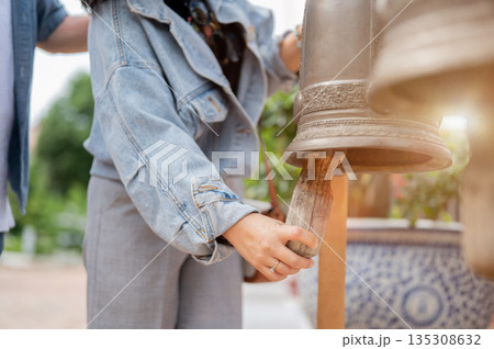 Close up of a woman in denim jacket ringing a brass bell for luck and prosperity at buddhist temple. 135308632