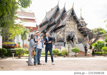 Old white man pointing with woman and Thai guide looking standing together in buddhist temple ground 135308636