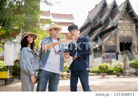 Old white man holding phone talk to asian guide with woman standing aside in buddhist temple grounds 135308651