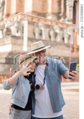 Old white man holding phone taking photo with smiling asian woman standing aside a pagoda in temple. Old white man holding phone taking photo with smiling asian woman standing aside a pagoda in temple. 135308661
