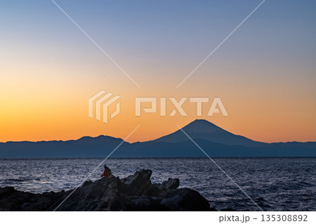 夕焼けの岩礁に立つ釣り人と海の向こうの富士山 夕焼けの岩礁に立つ釣り人と海の向こうの富士山 135308892