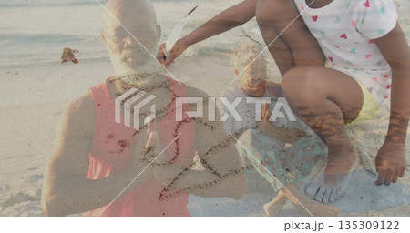 Family meditating and praying on sandy shoreline, with child tracing heart shape with feather 135309122