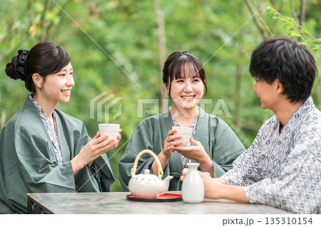 旅館・温泉旅館に旅行,社員旅行に来てテラスでお茶を飲む若い男女（トラベル） 135310154