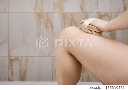 Woman dry brushing her leg, promoting skin blood circulation and exfoliation for wellness 135310381