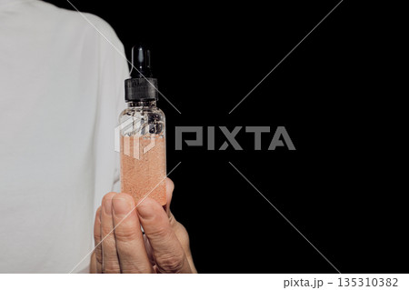 Hand holding glass dropper bottle containing skincare serum against black background 135310382