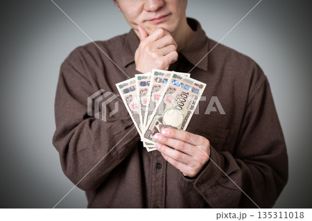 お金を持って悩むカジュアル姿のミドル男性ビジネスマン お金を持って悩むカジュアル姿のミドル男性ビジネスマン 135311018