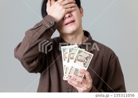 お金を持って悩むカジュアル姿のミドル男性ビジネスマン 135311056