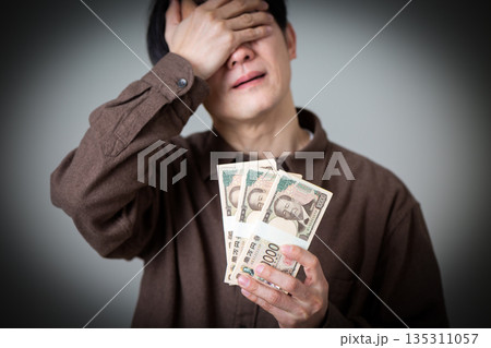お金の札束を持って悩むカジュアル姿のミドル男性ビジネスマン 135311057