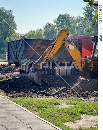 Excavator digging at a construction site with a truck nearby. 135311697