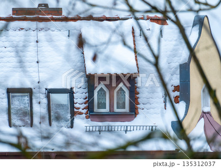 A view of a tiled roof covered in a thick layer of fluffy snow. Traditional architecture, dormers, and a wintry atmosphere in the city. 135312037