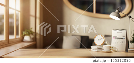 A clock atop books with coffee cup and calendar aside lamp on wooden table in a room with sunlight. A clock atop books with coffee cup and calendar aside lamp on wooden table in a room with sunlight. 135312056
