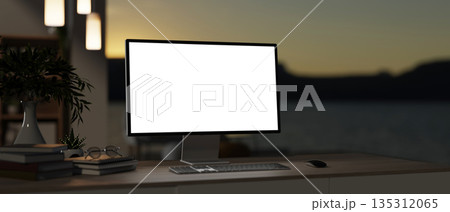 Blank screen computer with book and houseplant on wooden table in dim lit room with outside scenery. 135312065