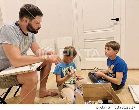 boys helping his father assemble a new piece of furniture with a screwdriver boys helping his father assemble a new piece of furniture with a screwdriver 135312517