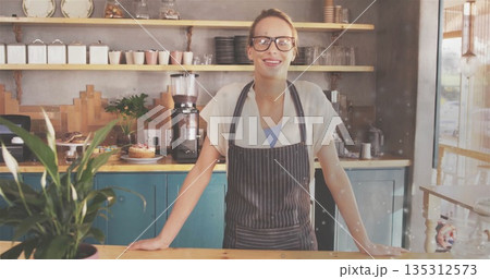 Standing woman wearing striped apron working behind wooden counter at coffee shop, with grinder Standing woman wearing striped apron working behind wooden counter at coffee shop, with grinder 135312573