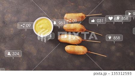 Displaying four corn dogs on wooden skewers on dark stone tabletop, with digital overlay icons 135312593